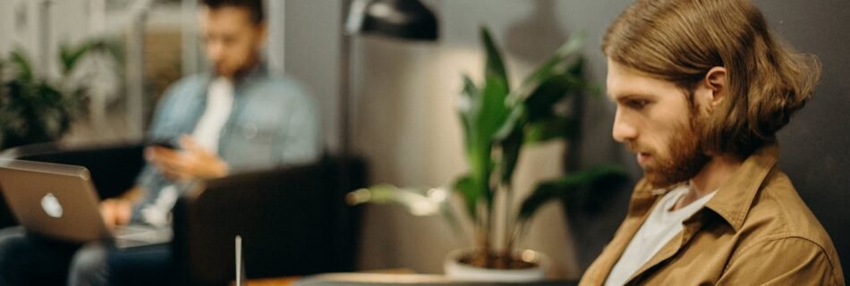 Two men using laptops in a modern office, emphasizing remote work trends.