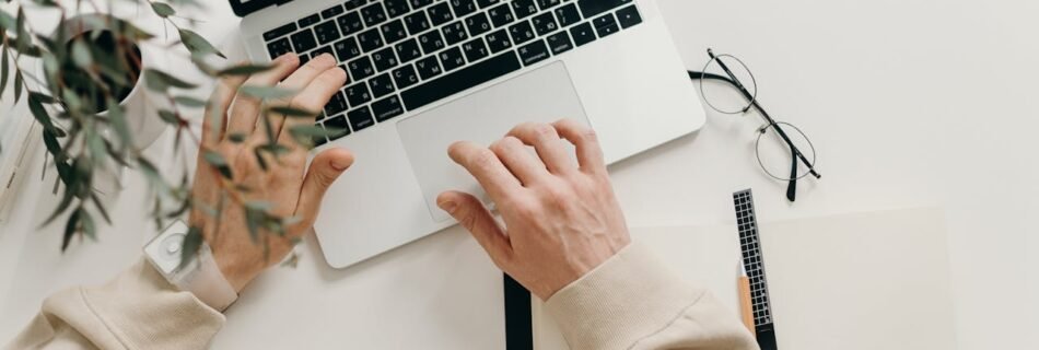 An overhead view of a person working on a laptop in a minimalist home office setting.