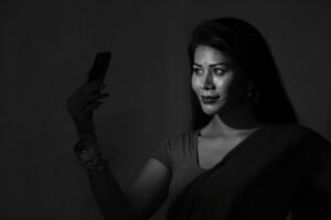 Black and white portrait of an Indian woman in a sari taking a selfie, highlighting grace and technology.